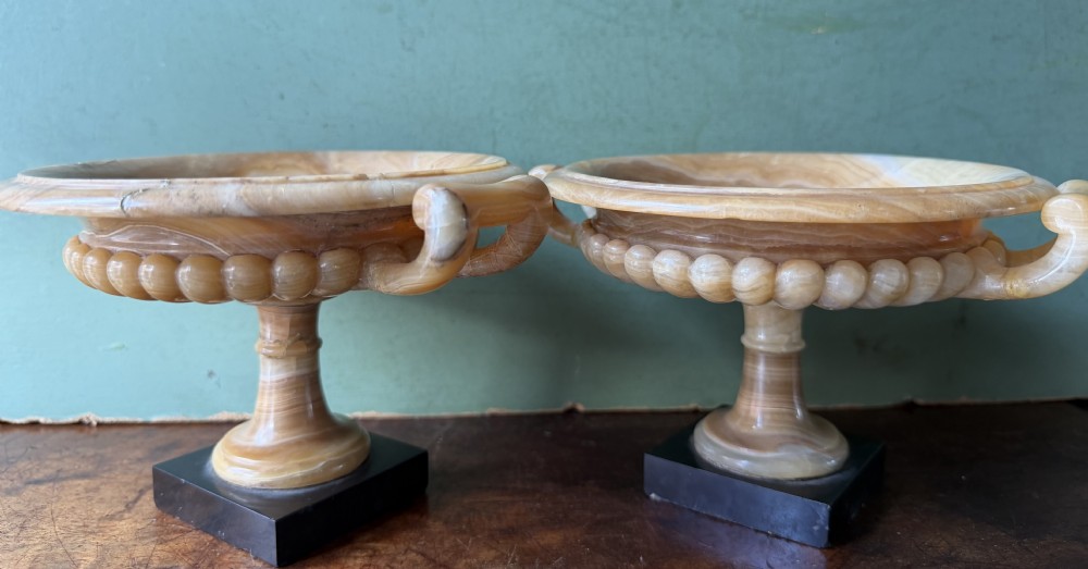 A pair of 19th-century carved amber alabaster tazze with gadrooned rims and twin loop handles set on square black marble plinths. View XX