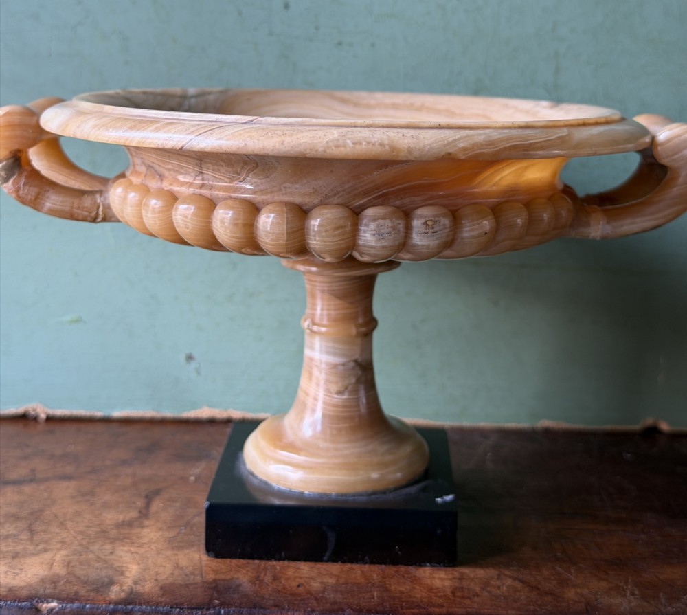 A pair of 19th-century carved amber alabaster tazze with gadrooned rims and twin loop handles set on square black marble plinths. View XXIII