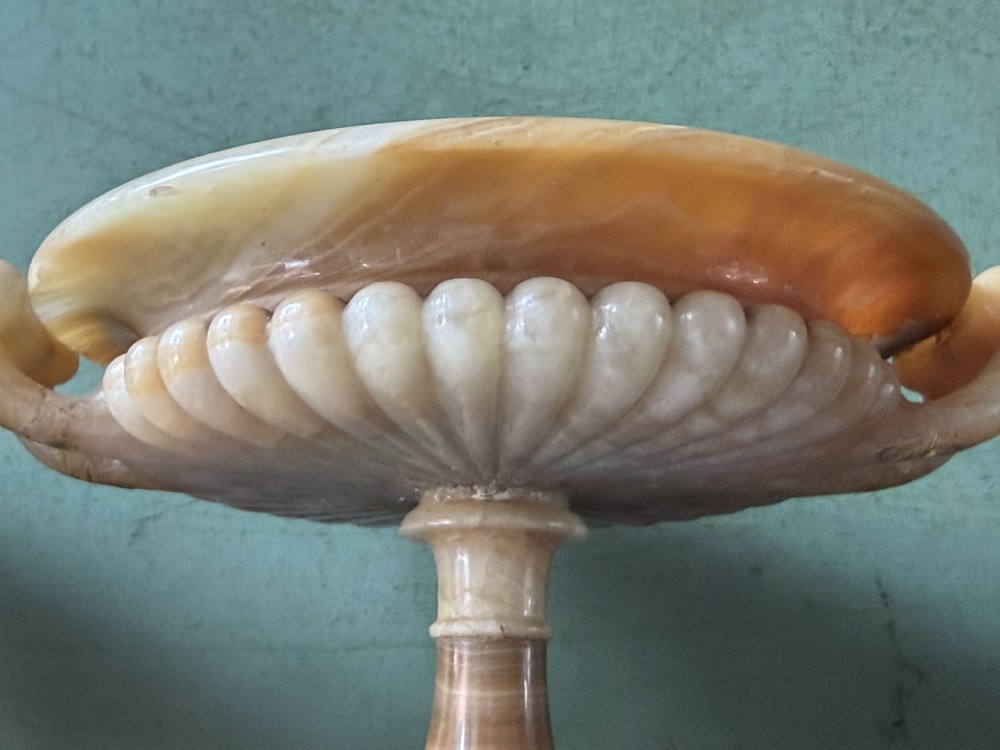 A pair of 19th-century carved amber alabaster tazze with gadrooned rims and twin loop handles set on square black marble plinths. View XXIV