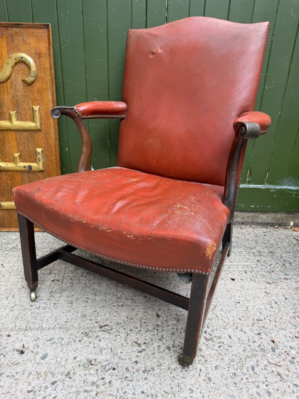 An 18th-century George III Gainsborough library armchair upholstered in aged red leather with a mahogany frame, padded armrests, brass stud trim, and brass castors.