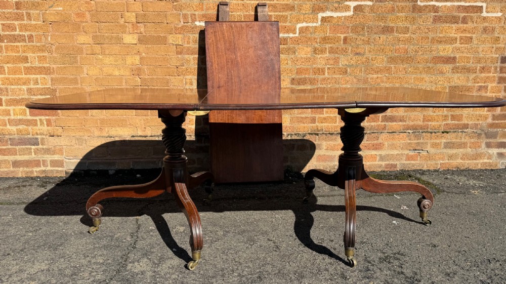 An early 19th-century George III twin-pillar mahogany dining table featuring reeded splayed legs and original brass castors. View II