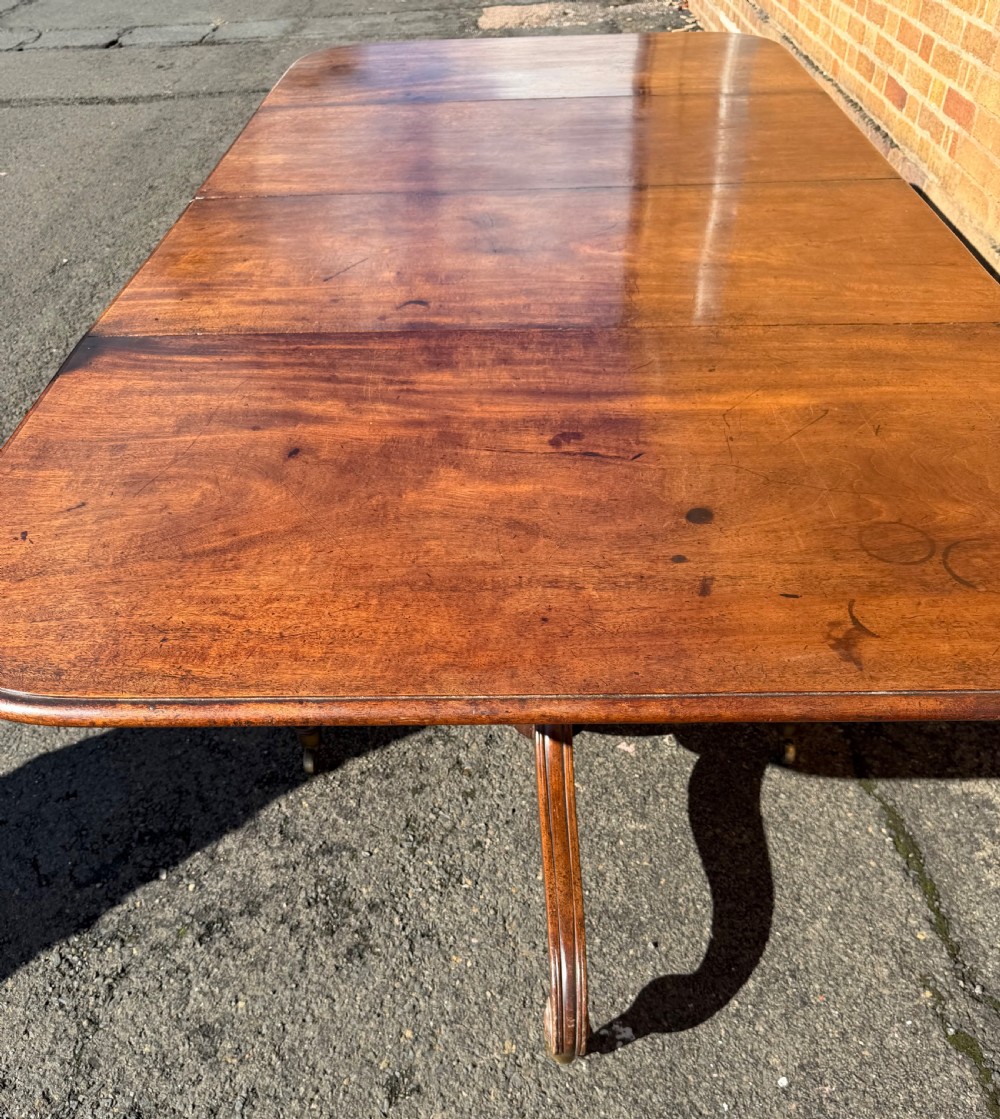 An early 19th-century George III twin-pillar mahogany dining table featuring reeded splayed legs and original brass castors. View XI