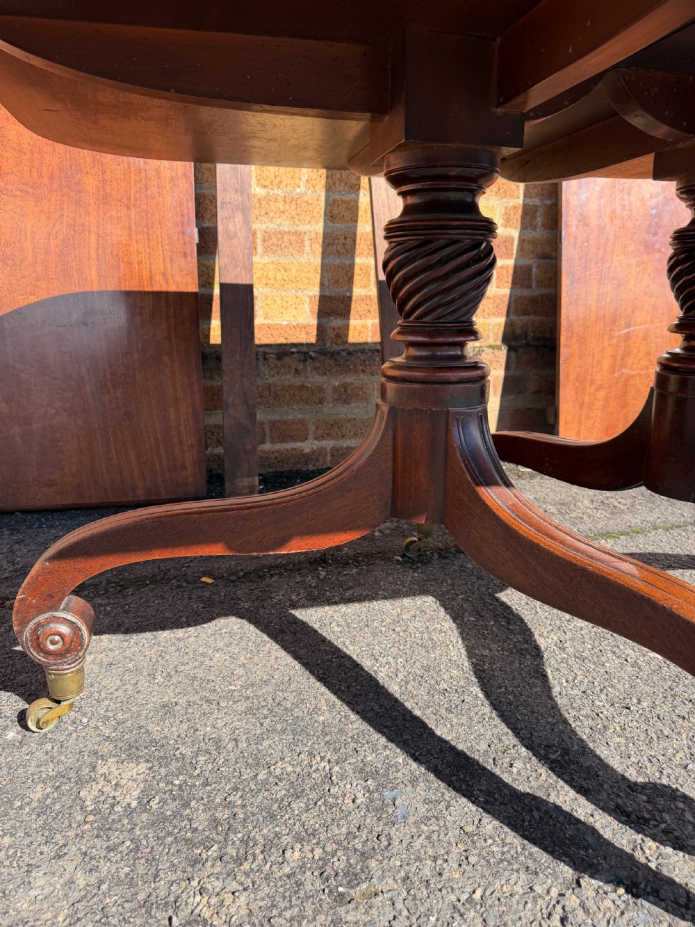 An early 19th-century George III twin-pillar mahogany dining table featuring reeded splayed legs and original brass castors. View XIX