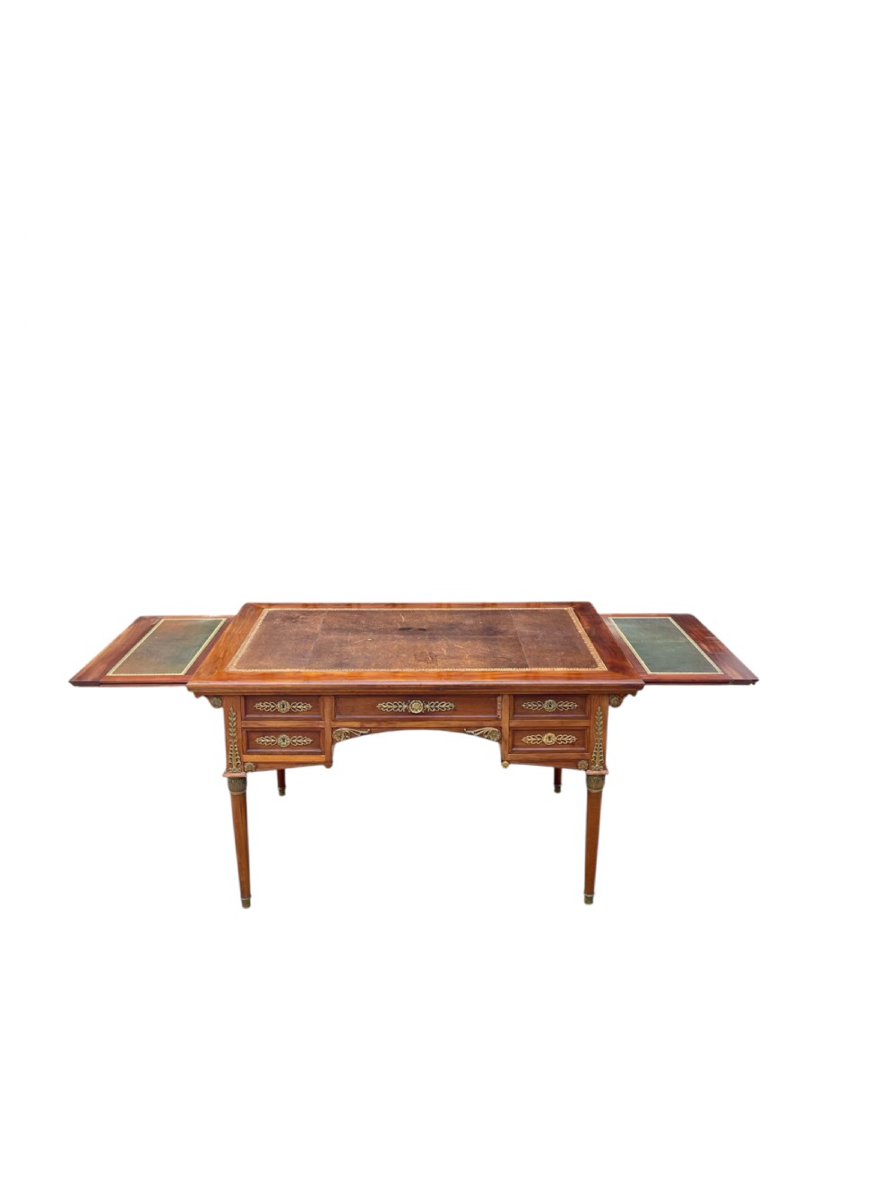 A French Empire style mahogany writing desk featuring a gilt-tooled leather writing surface, pull-out side slides, ormolu brass mounts, and tapered legs.