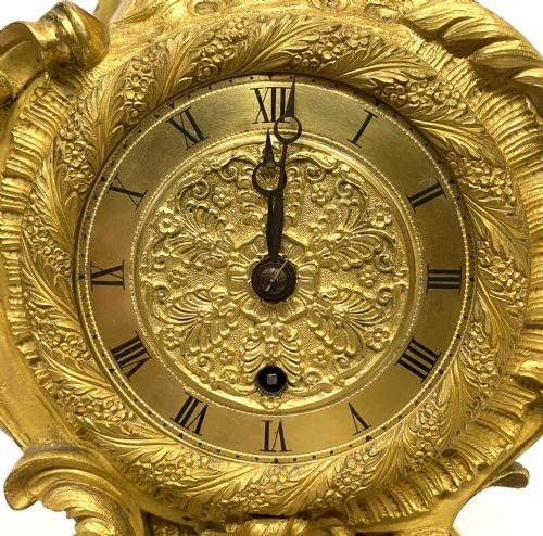 fig 2. A Rococo style gilt bronze mantel clock featuring scrollwork, acanthus leaf carving, and a gilded dial with Roman numerals.