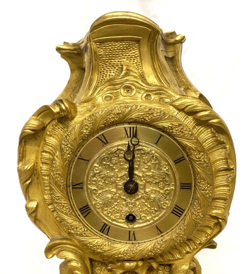 fig 3. A Rococo style gilt bronze mantel clock featuring scrollwork, acanthus leaf carving, and a gilded dial with Roman numerals.