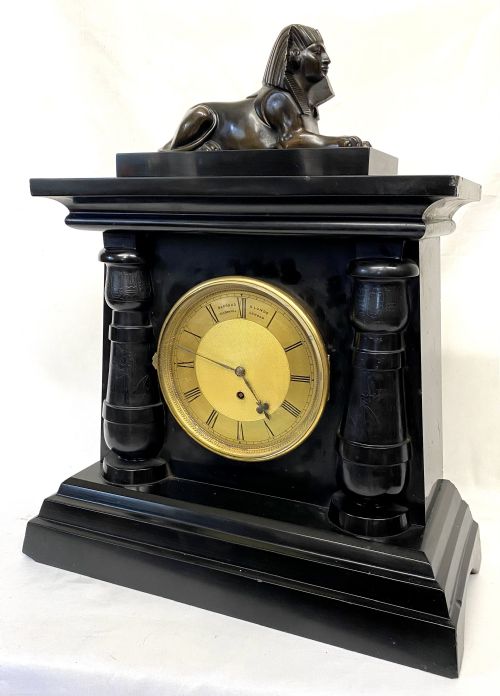 fig 1. An antique black slate mantel clock in the Egyptian Revival style, featuring a bronze sphinx atop the case and engraved columns framing a circular brass dial.