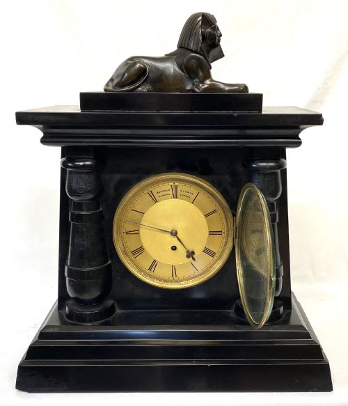 fig 2. An antique black slate mantel clock in the Egyptian Revival style, featuring a bronze sphinx atop the case and engraved columns framing a circular brass dial.