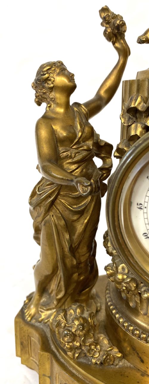 fig 1. An ornate gilt bronze miniature mantel clock featuring figures of a classical maiden and two winged cherubs surrounding a white enamel dial.