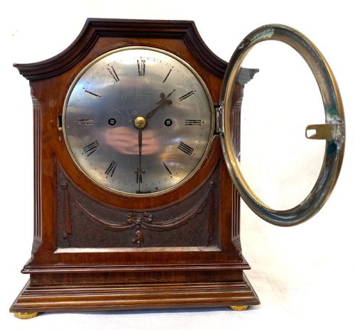 fig 2. An antique mahogany double chain fusee mantel clock featuring a curved pediment, fluted side columns, carved drapery swag panel, and a silvered dial with Roman numerals.