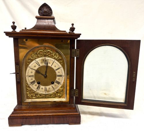 fig 2. An antique walnut bracket clock featuring an arched brass dial with decorative corner spandrels, Roman numerals, and turned finials on a stepped wood base.