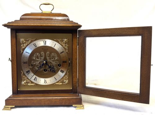 fig 2. A burr walnut basket top mantel clock featuring an etched brass dial with Roman numerals, corner spandrels, side glass panels, and a top brass handle.