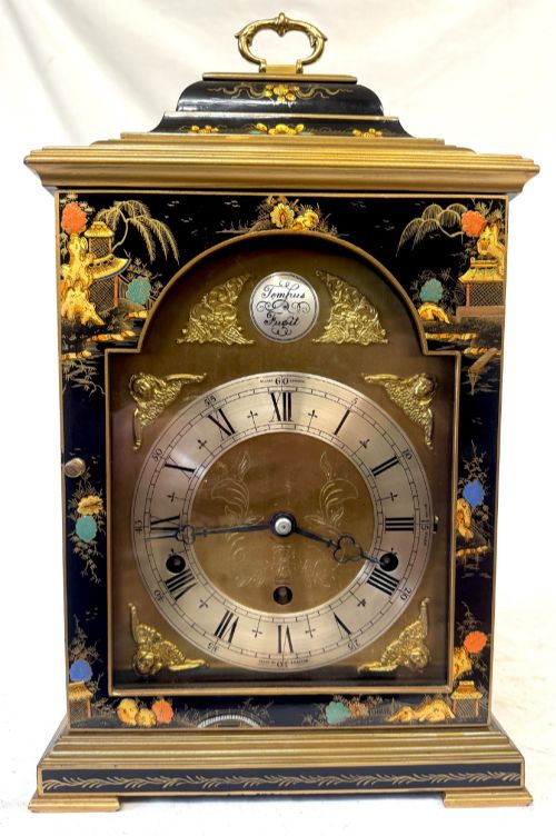 fig 1. A black lacquered chinoiserie bracket clock featuring hand-painted gilt landscape scenes, a brass dial with Roman numerals, and a top brass carrying handle.