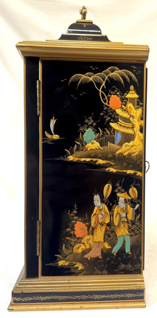 A black lacquered chinoiserie bracket clock featuring hand-painted gilt landscape scenes, a brass dial with Roman numerals, and a top brass carrying handle. View VI