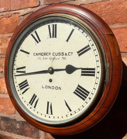 fig 1. A circular Victorian mahogany wall clock with a cream painted dial displaying Roman numerals, makers inscription for Camerer Cuss & Co London, and a brass bezel.
