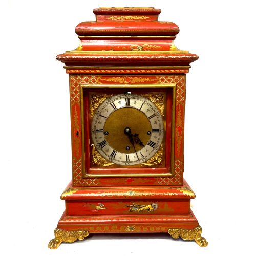 fig 1. A red lacquered bracket clock decorated with gold chinoiserie motifs, featuring a brass dial and gilt metal feet.