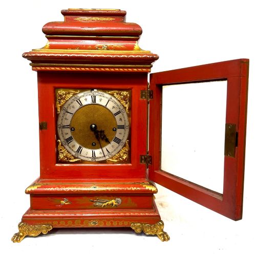 fig 2. A red lacquered bracket clock decorated with gold chinoiserie motifs, featuring a brass dial and gilt metal feet.