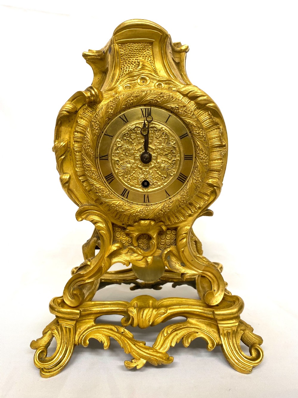 A Rococo style gilt bronze mantel clock featuring scrollwork, acanthus leaf carving, and a gilded dial with Roman numerals.