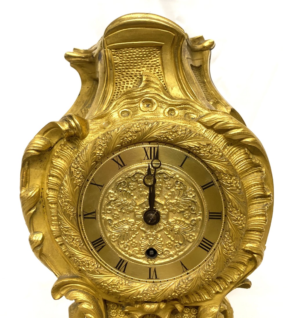 A Rococo style gilt bronze mantel clock featuring scrollwork, acanthus leaf carving, and a gilded dial with Roman numerals. View IV