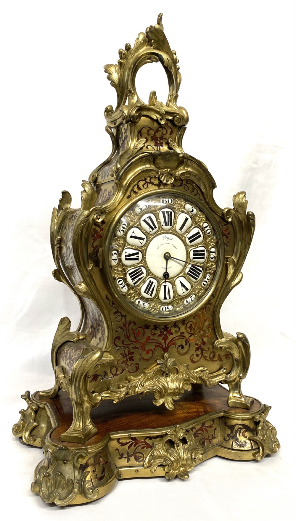 An ornate Rococo Revival mantel clock featuring brass and tortoiseshell Boulle marquetry inlay, gilt mounts, and individual white enamel cartouche Roman numerals on a matching plinth base.