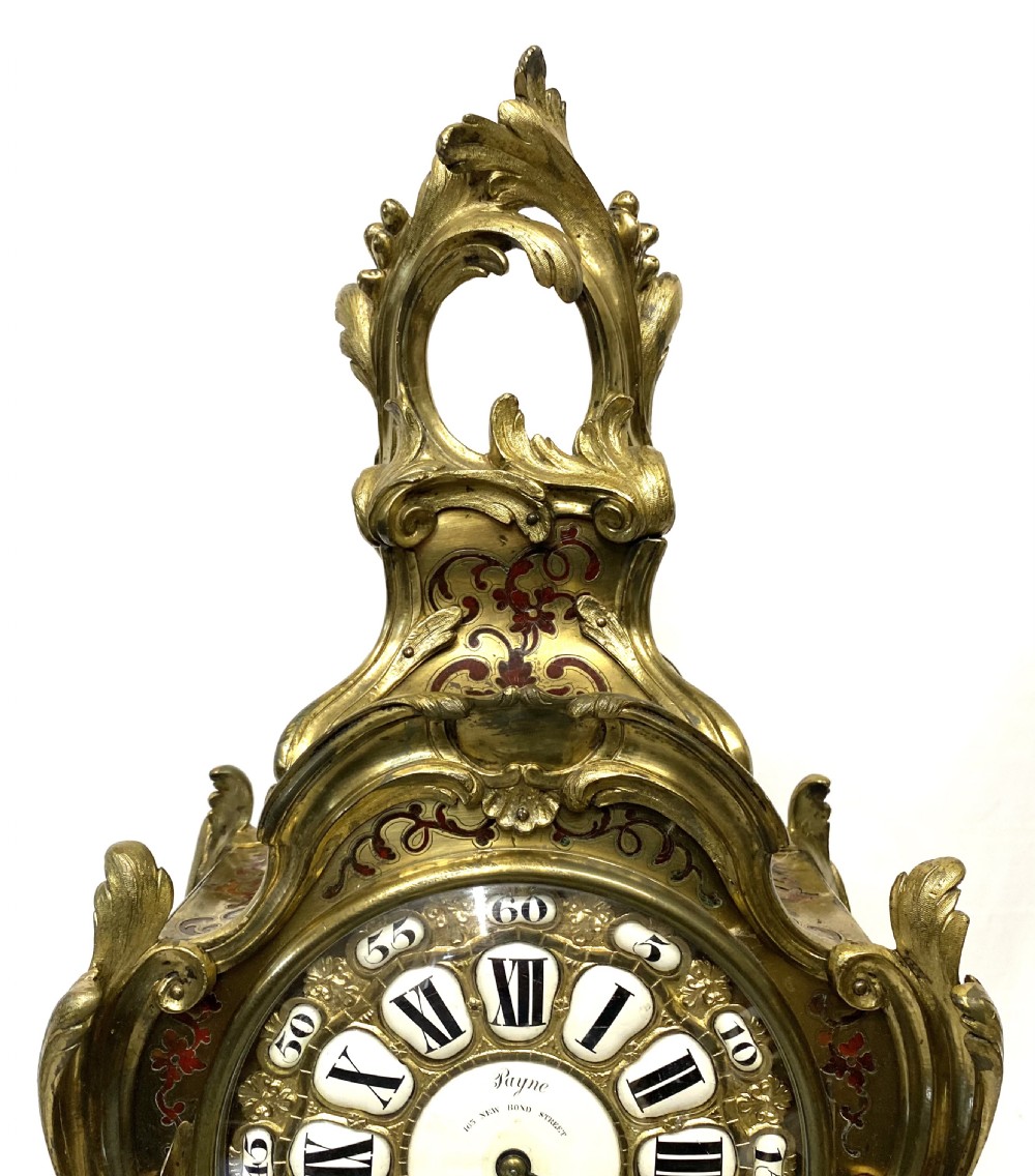 An ornate Rococo Revival mantel clock featuring brass and tortoiseshell Boulle marquetry inlay, gilt mounts, and individual white enamel cartouche Roman numerals on a matching plinth base. View VI