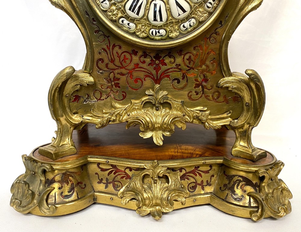 An ornate Rococo Revival mantel clock featuring brass and tortoiseshell Boulle marquetry inlay, gilt mounts, and individual white enamel cartouche Roman numerals on a matching plinth base. View VII
