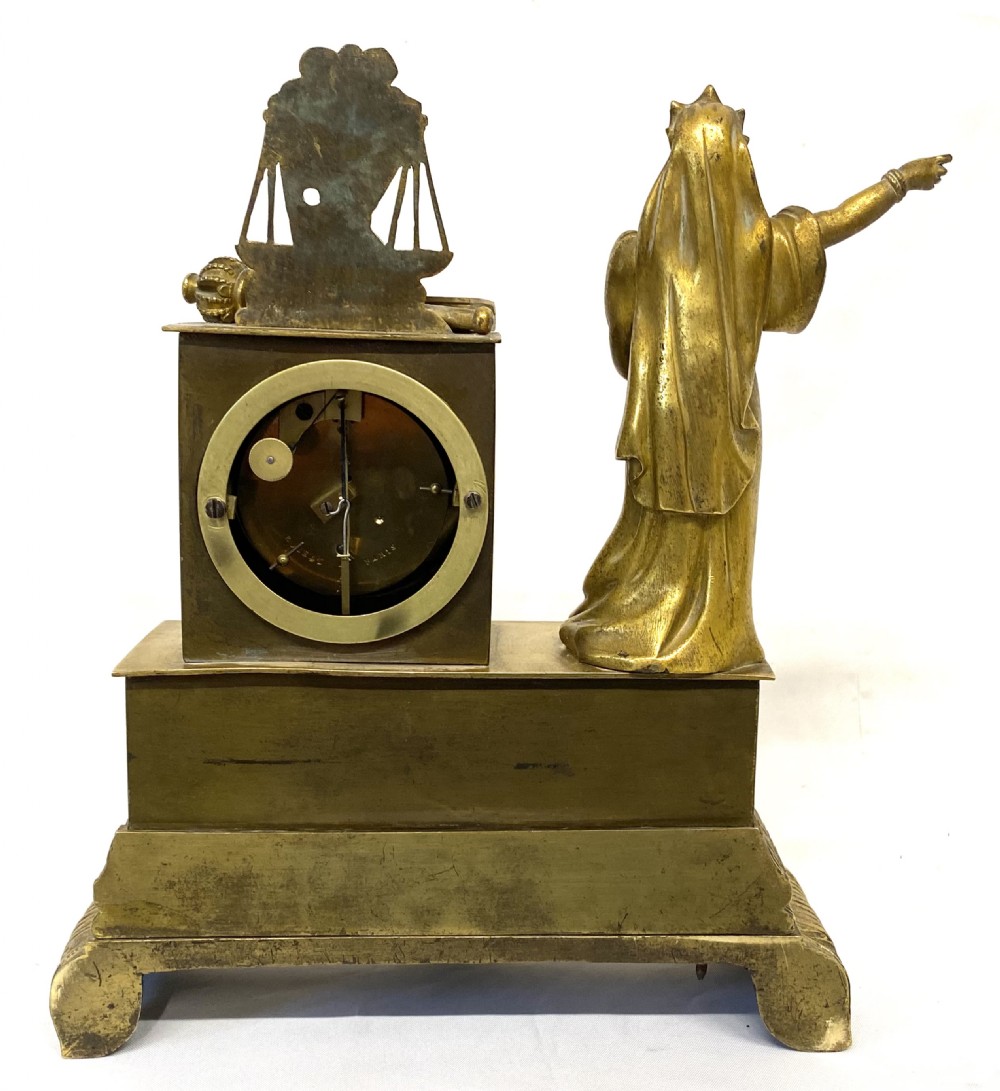A nineteenth-century French gilt bronze mantel clock featuring a standing female figure beside a square clock casing surmounted by scales of justice. View X
