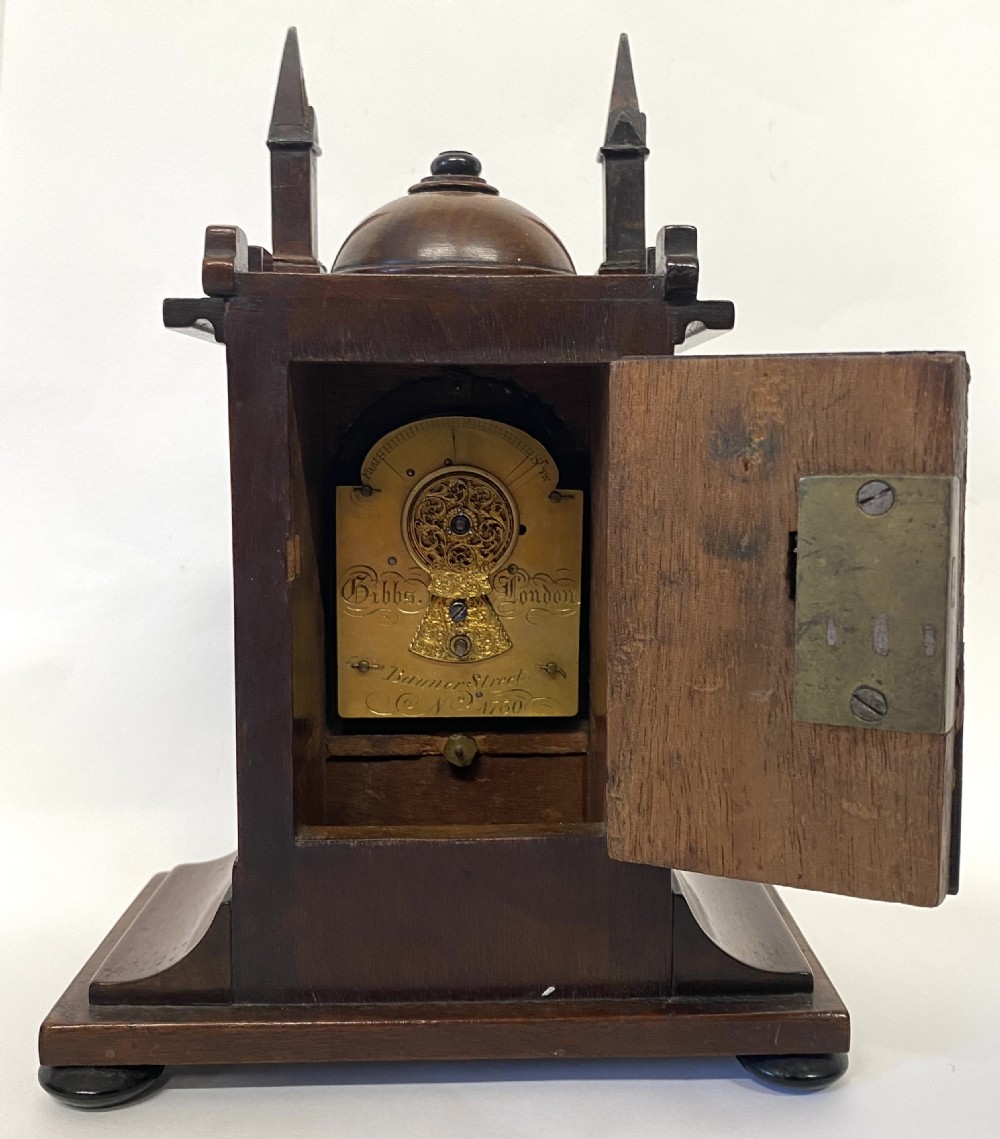 A miniature architectural mahogany mantel clock with corner spires, a domed roof, and an engraved brass dial with Roman numerals. View VII