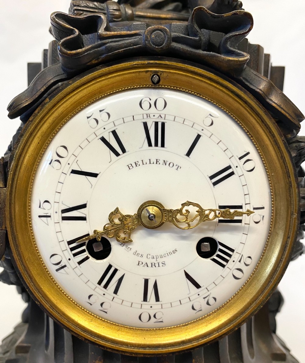 An antique dark patinated bronze mantel clock topped with a seated cherub figure above a fluted cylindrical base and white enamel dial signed Bellenot Paris. View IV