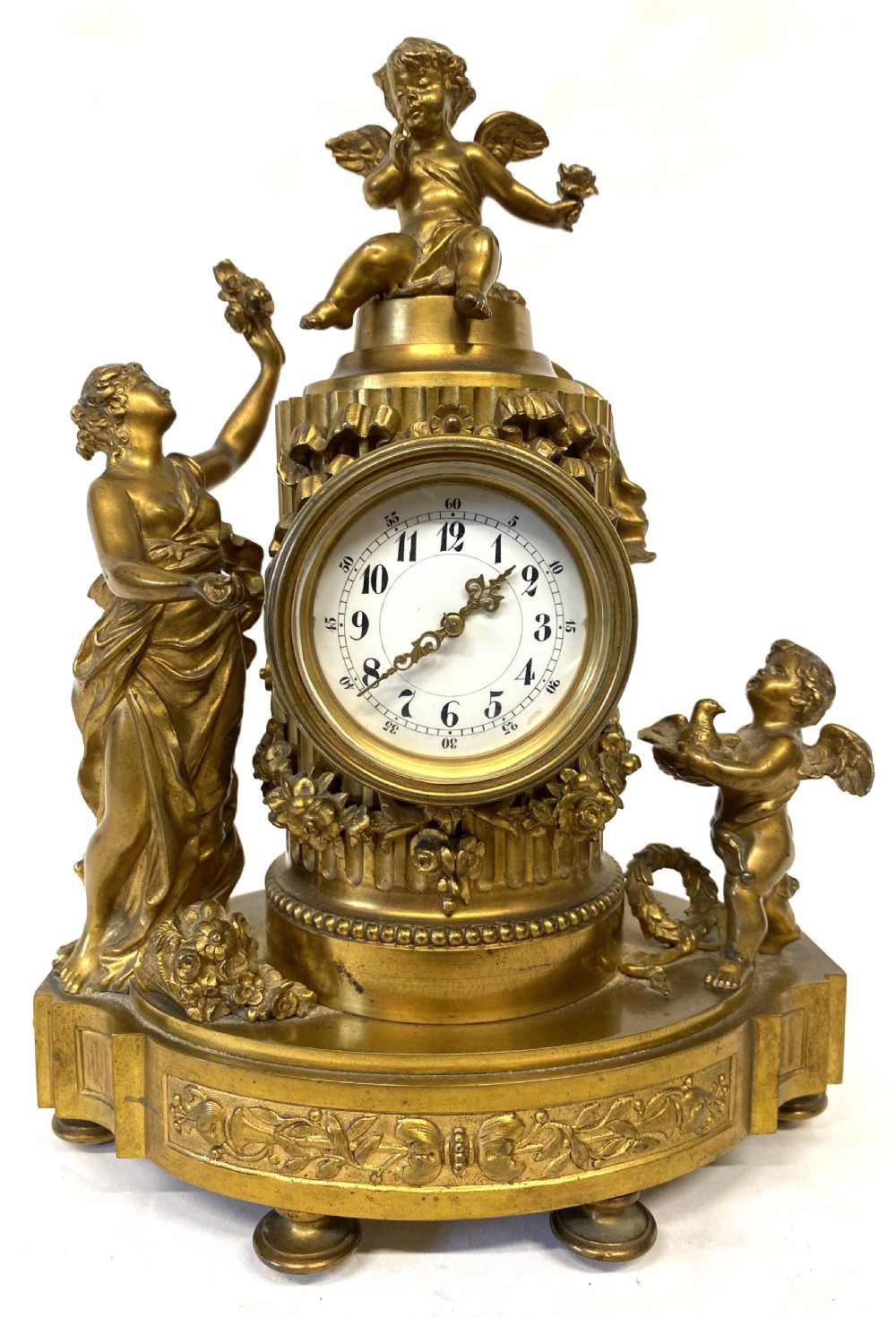 An ornate gilt bronze miniature mantel clock featuring figures of a classical maiden and two winged cherubs surrounding a white enamel dial. View III