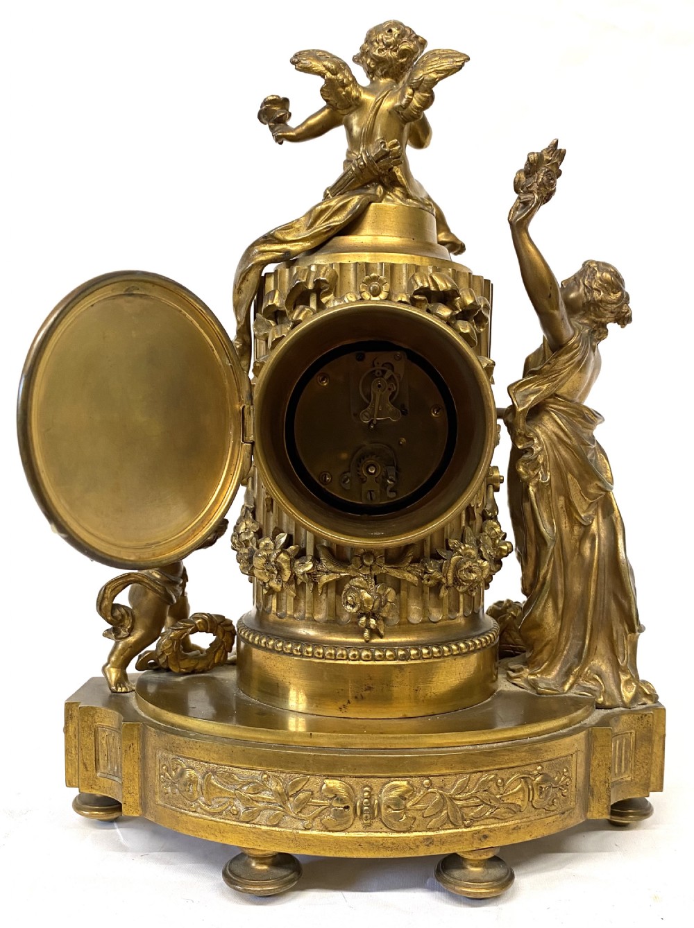 An ornate gilt bronze miniature mantel clock featuring figures of a classical maiden and two winged cherubs surrounding a white enamel dial. View XI