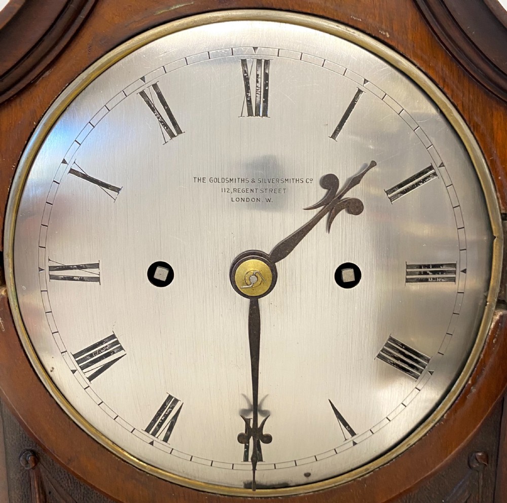 An antique mahogany double chain fusee mantel clock featuring a curved pediment, fluted side columns, carved drapery swag panel, and a silvered dial with Roman numerals. View IV