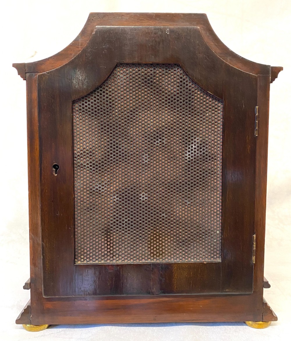 An antique mahogany double chain fusee mantel clock featuring a curved pediment, fluted side columns, carved drapery swag panel, and a silvered dial with Roman numerals. View VII