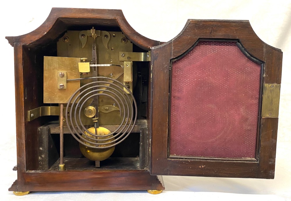 An antique mahogany double chain fusee mantel clock featuring a curved pediment, fluted side columns, carved drapery swag panel, and a silvered dial with Roman numerals. View VIII