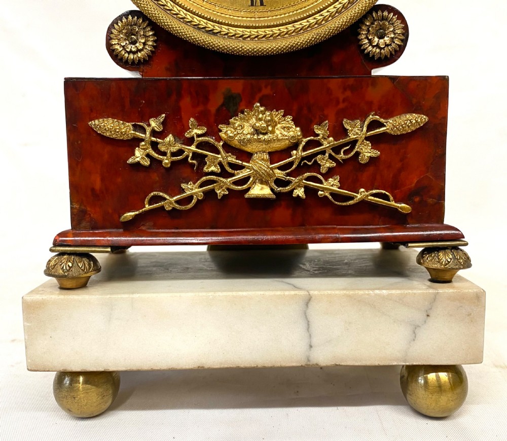 A Regency ormolu mantel clock with an engine-turned gold dial, floral gilt mounts, and a white marble plinth resting on brass feet. View IV