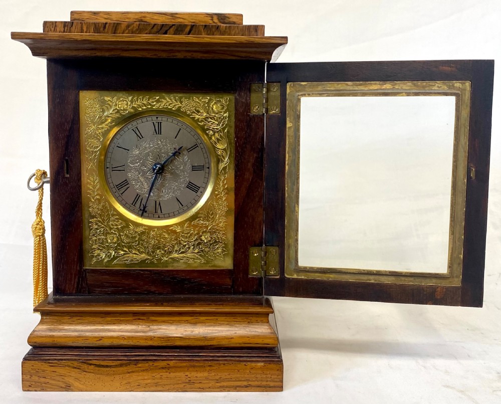 An antique rosewood library table clock featuring glazed side panels, an engraved brass face with Roman numerals, and a stepped wooden base. View III
