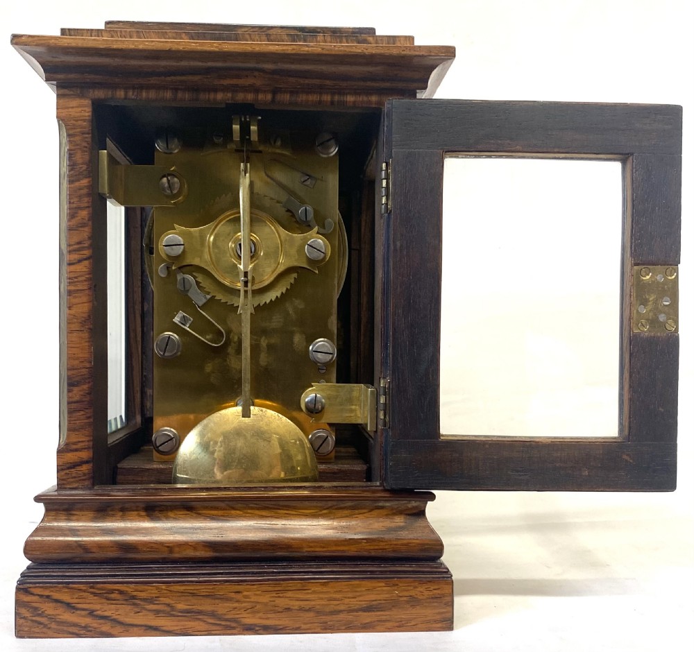 An antique rosewood library table clock featuring glazed side panels, an engraved brass face with Roman numerals, and a stepped wooden base. View XI