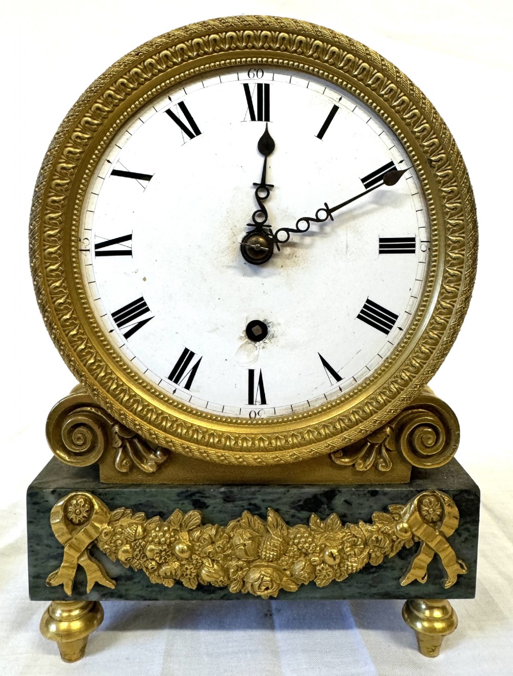 A Regency mantel clock featuring a white enamel dial with Roman numerals set above a green marble base adorned with gilt-bronze floral swags. View II