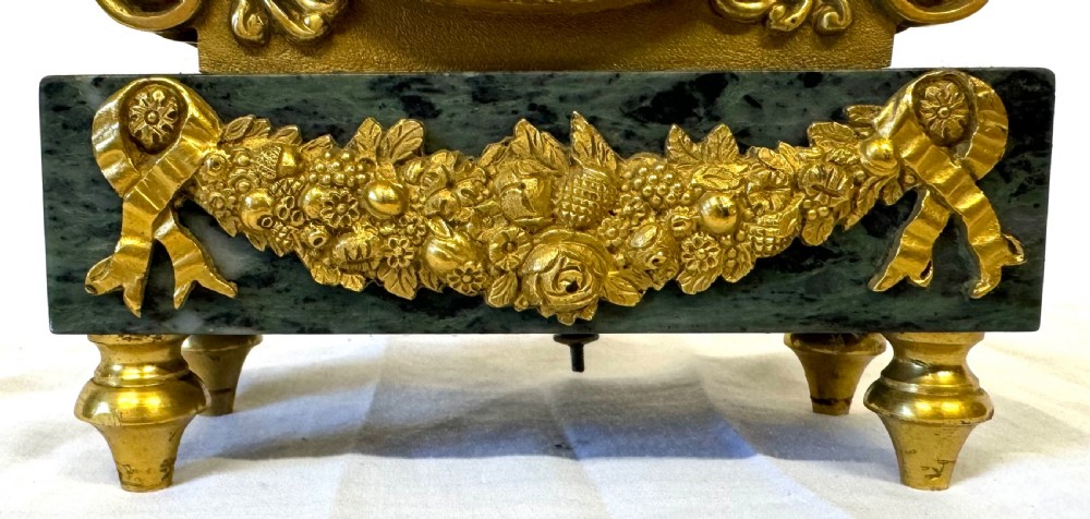 A Regency mantel clock featuring a white enamel dial with Roman numerals set above a green marble base adorned with gilt-bronze floral swags. View IV