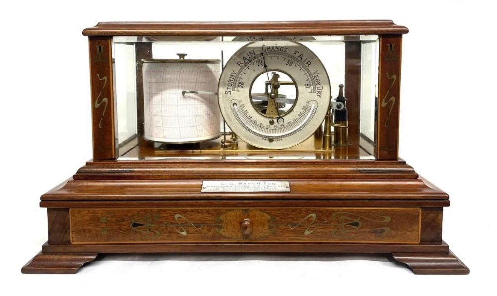 An Art Nouveau mahogany barograph featuring a glazed display case, stylized inlay on the timber frame and base drawer, an internal recording drum, and a silvered barometer dial.