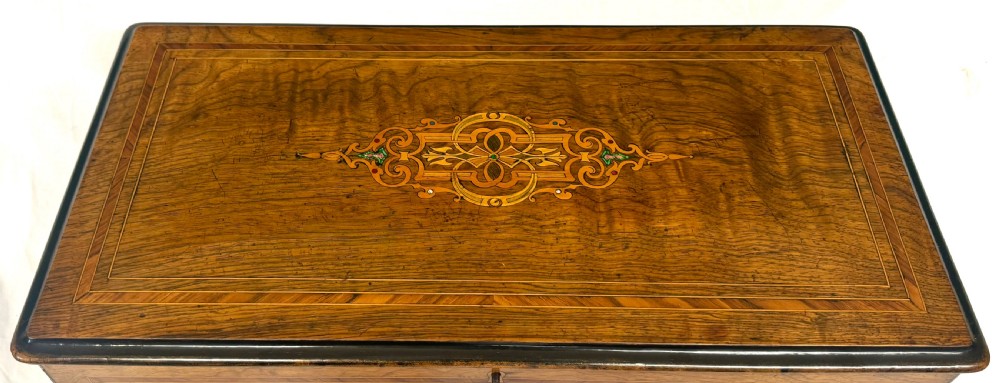An antique rectangular wooden music box featuring floral marquetry inlay on the lid and front, framed by dark ebonised edges with a key inserted in the lock. View II