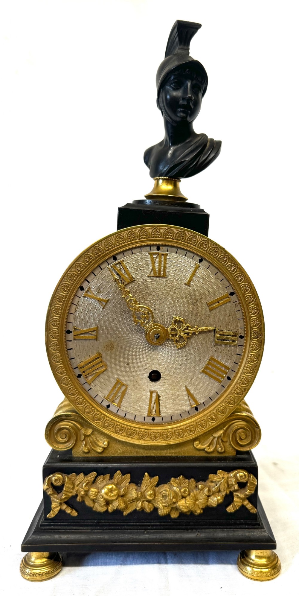 A Regency period mantel clock featuring a dark patinated classical bust above a gilded engine-turned dial, resting on a black rectangular base with gilded floral mounts and turned feet. View III