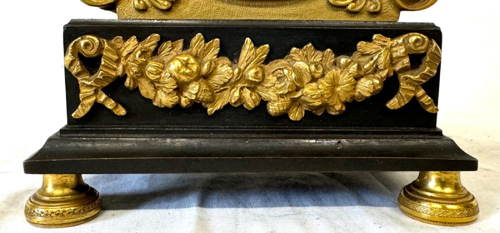 A Regency period mantel clock featuring a dark patinated classical bust above a gilded engine-turned dial, resting on a black rectangular base with gilded floral mounts and turned feet. View IV