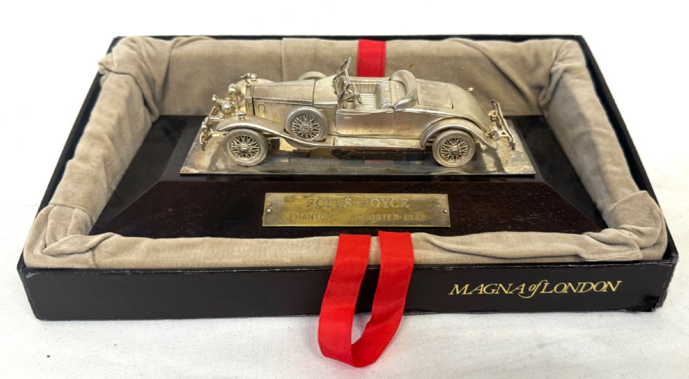 A solid silver model of a classic Rolls Royce Phantom II roadster mounted on a dark wooden plinth inside a presentation box. View II