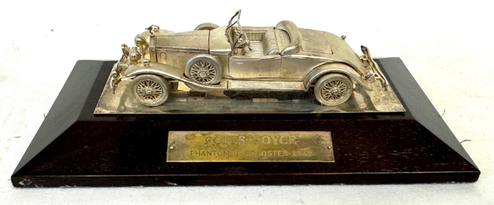 A solid silver model of a classic Rolls Royce Phantom II roadster mounted on a dark wooden plinth inside a presentation box. View III