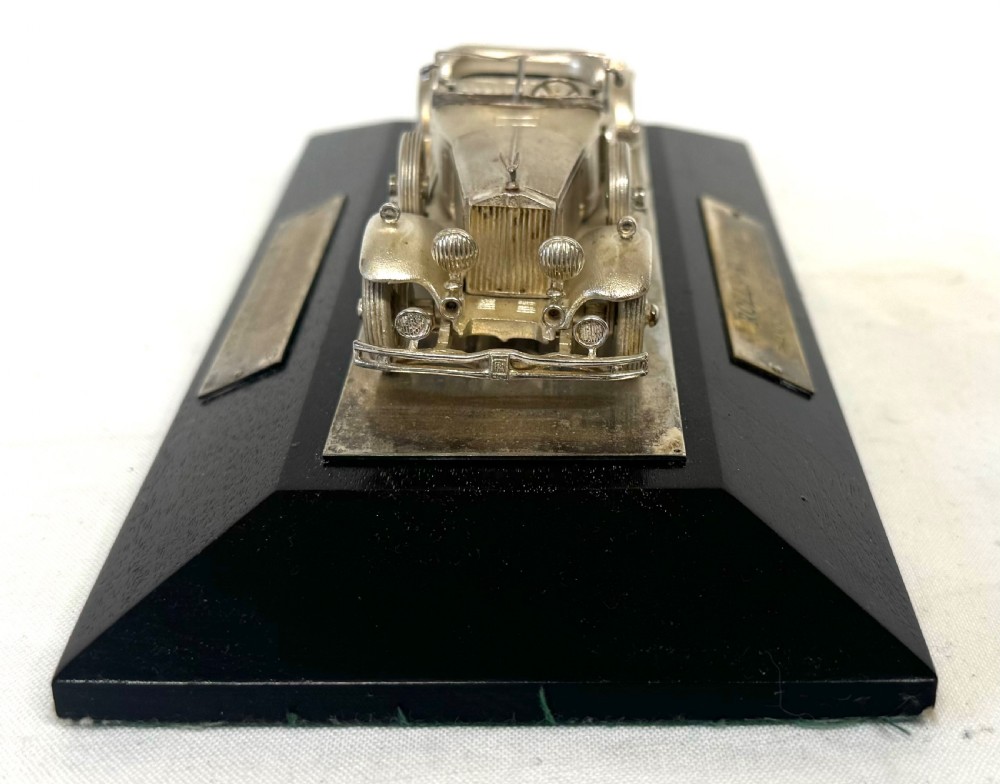 A solid silver model of a classic Rolls Royce Phantom II roadster mounted on a dark wooden plinth inside a presentation box. View V