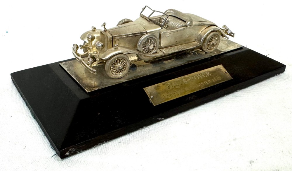 A solid silver model of a classic Rolls Royce Phantom II roadster mounted on a dark wooden plinth inside a presentation box. View VI