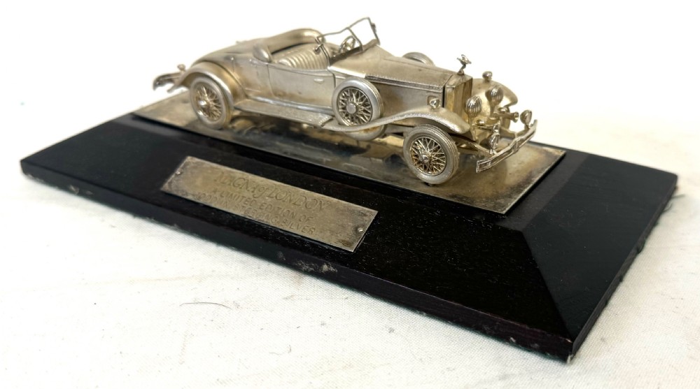 A solid silver model of a classic Rolls Royce Phantom II roadster mounted on a dark wooden plinth inside a presentation box. View VII