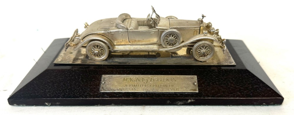 A solid silver model of a classic Rolls Royce Phantom II roadster mounted on a dark wooden plinth inside a presentation box. View VIII