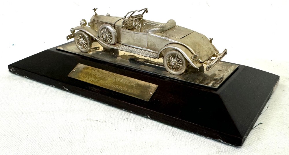 A solid silver model of a classic Rolls Royce Phantom II roadster mounted on a dark wooden plinth inside a presentation box. View XII